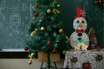Blackboard with child writing, christmas tree decorated, snow man made out of paper cups on a table wearing a red top hat